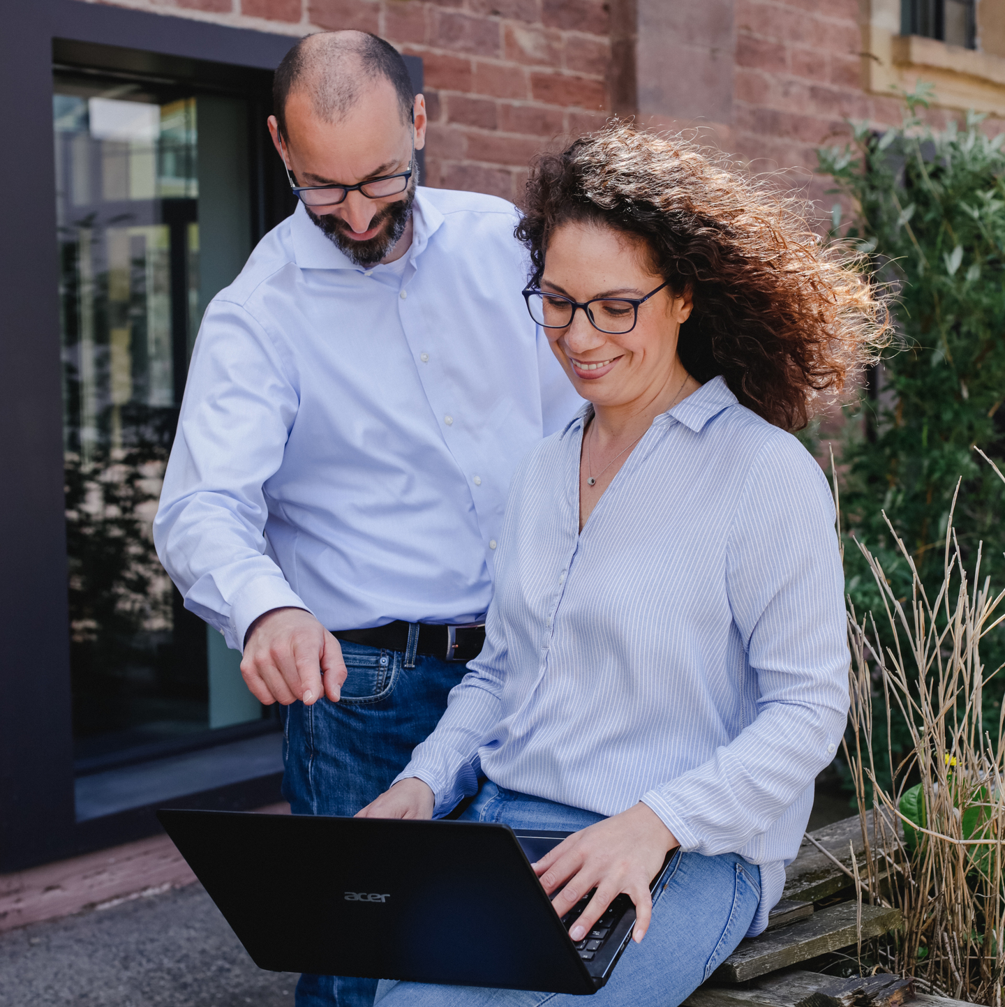 Zwei Personen, ein Mann und eine Frau, sitzen auf einer Bank und arbeiten gemeinsam an einem Laptop.